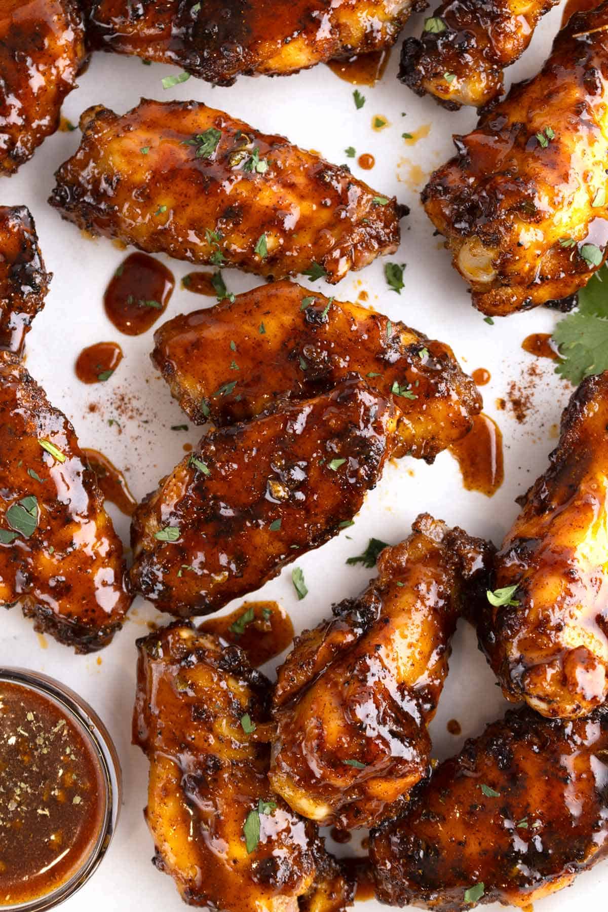 Honey chipotle sauce dripping off a cluster of chicken wings on a white surface.