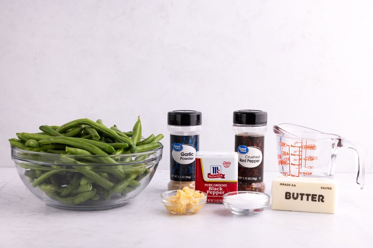 Green beans, garlic, seasonings, water, and butter on a white surface.