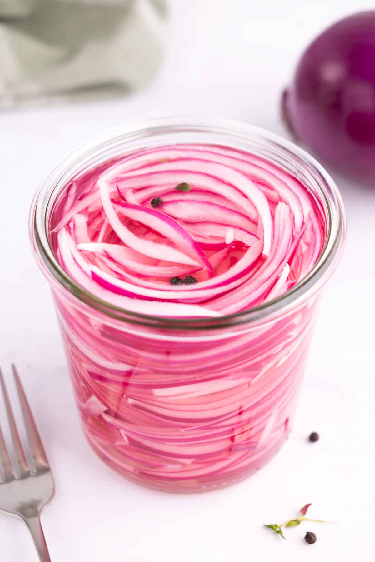 A jar of pickled red onions with a fork beside it.