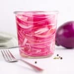 Onions in vinegar sitting in a small glass jar with a fork beside it.
