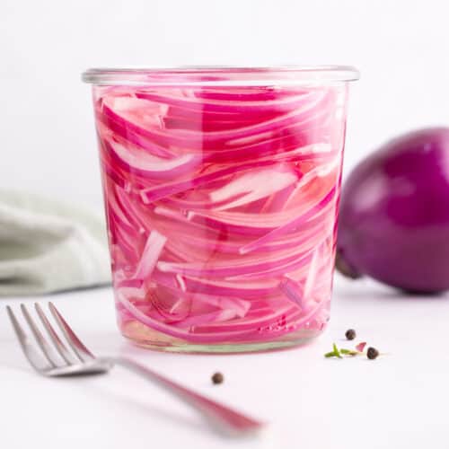 Onions in vinegar sitting in a small glass jar with a fork beside it.