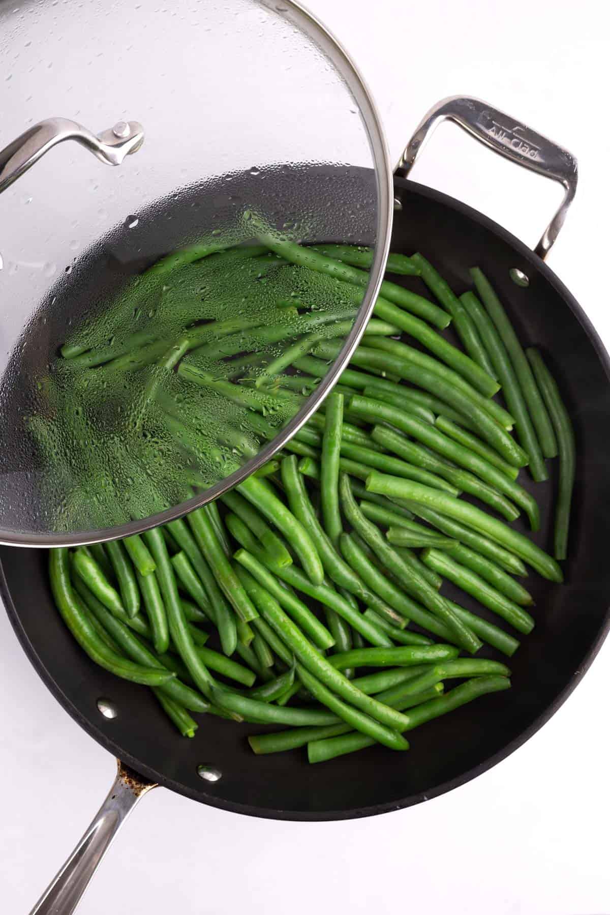 A pan of steamed green beans with the lid halfway over it.