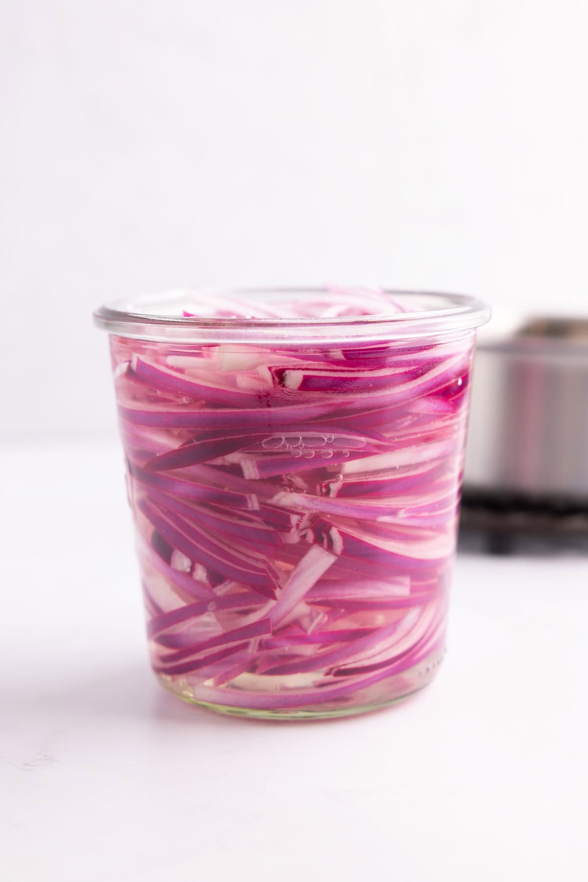 Pickled red onions in a glass cup.